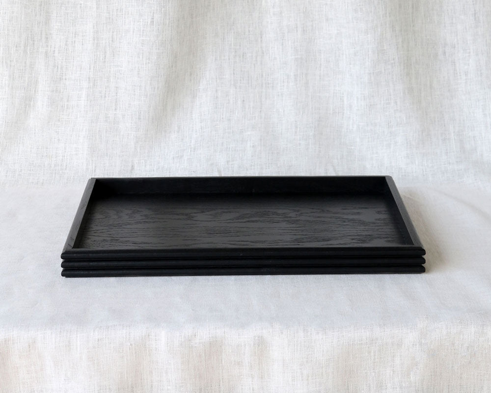 Front view of an empty rectangular black wooden tray, showcasing its minimalist design and stacked reeded edge detail.