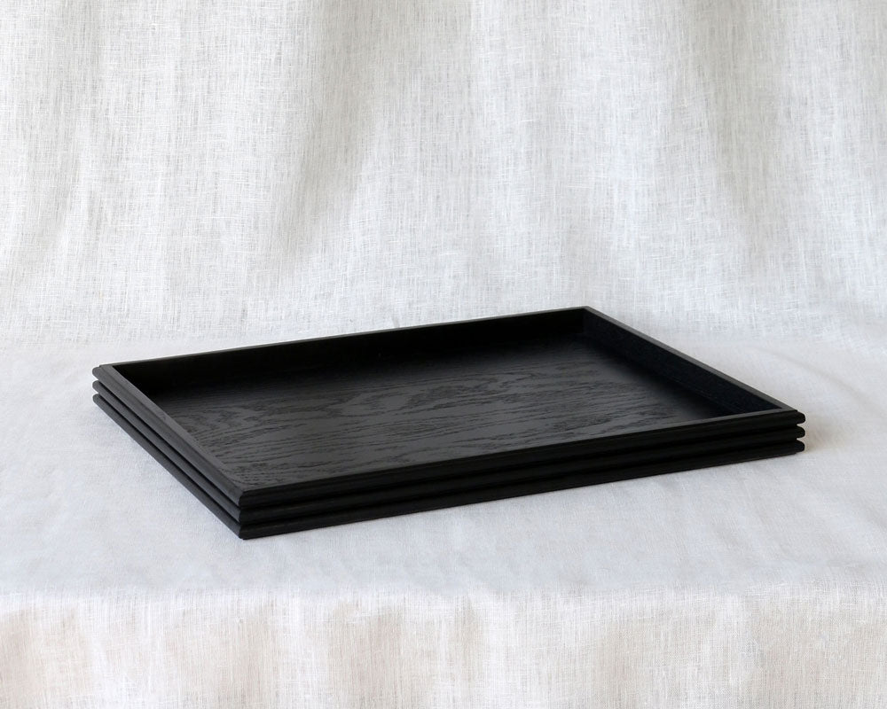 Angled side view of the black tray highlighting the clean lines, low-profile edge, and visible wood grain pattern