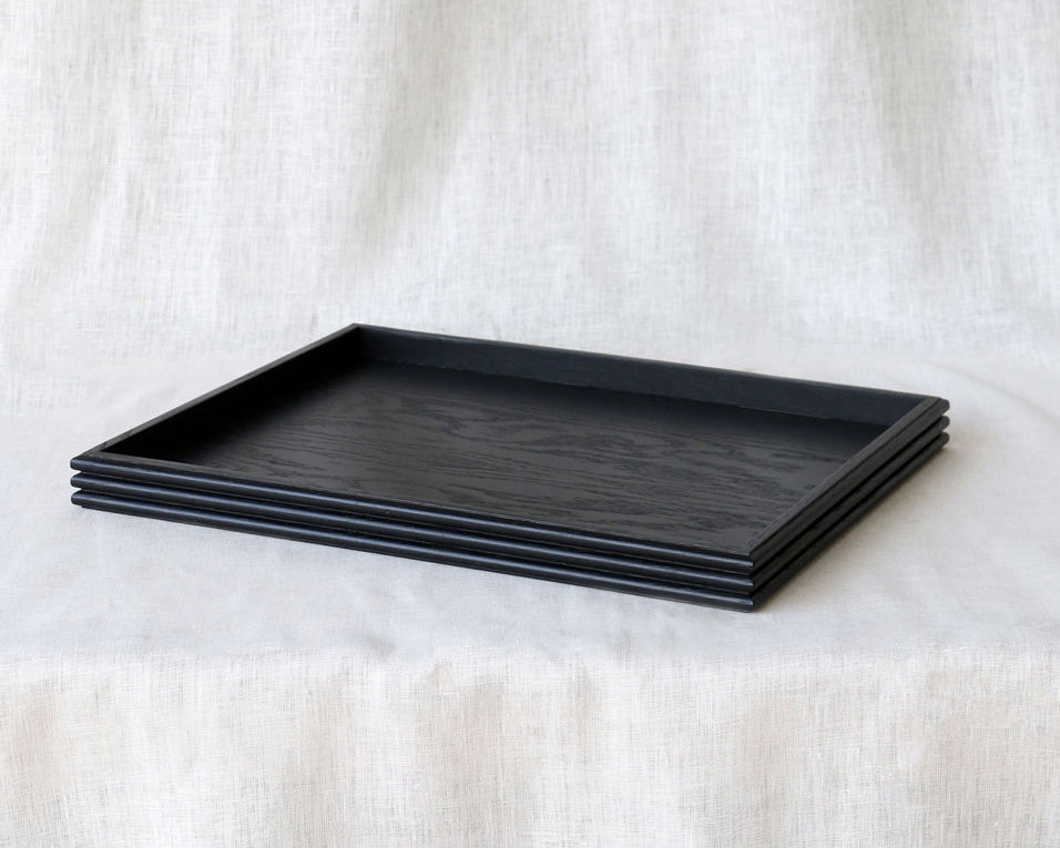 Three-quarter view of the black wooden tray resting on a linen-covered surface, emphasizing the handcrafted reeded edges and matte finish.