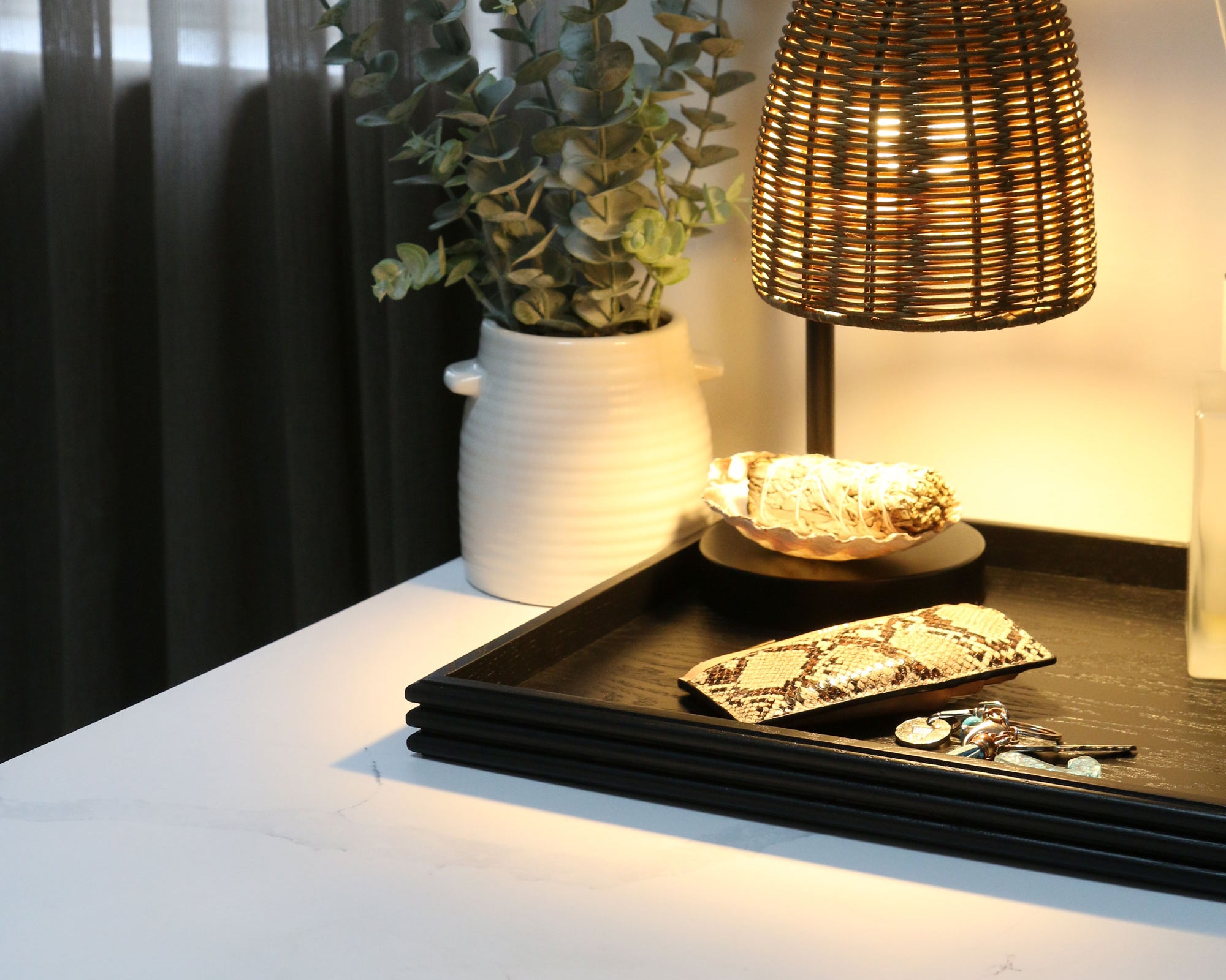 A coffee table tray in black wood, placed on a nightstand, holding keys, a wallet, and a book, serving as a stylish and functional bedside organizer.