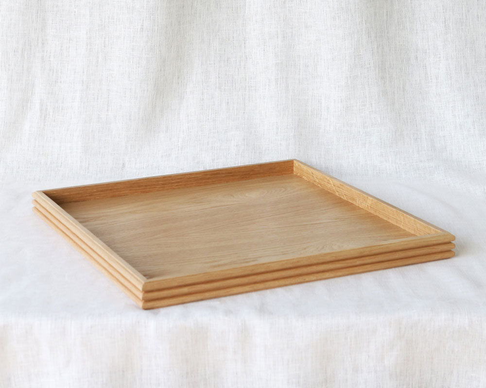 Angled shot of the empty oak tray, highlighting its minimalist design, raised edges, and reeded detail against a neutral fabric background.