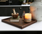 A coffee table tray in dark walnut, featuring elegant reeded edges, styled with books and a candle in a contemporary kitchen setting.