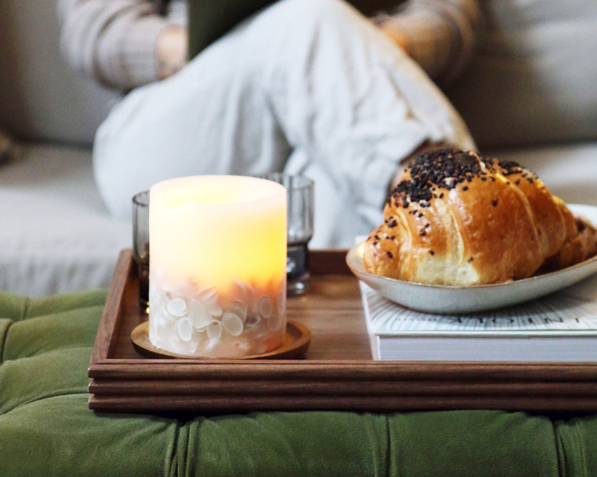 A wooden tray for a footstool, made from walnut with a deep, rich tone, styled with a glowing candle, adding warmth to the living space.