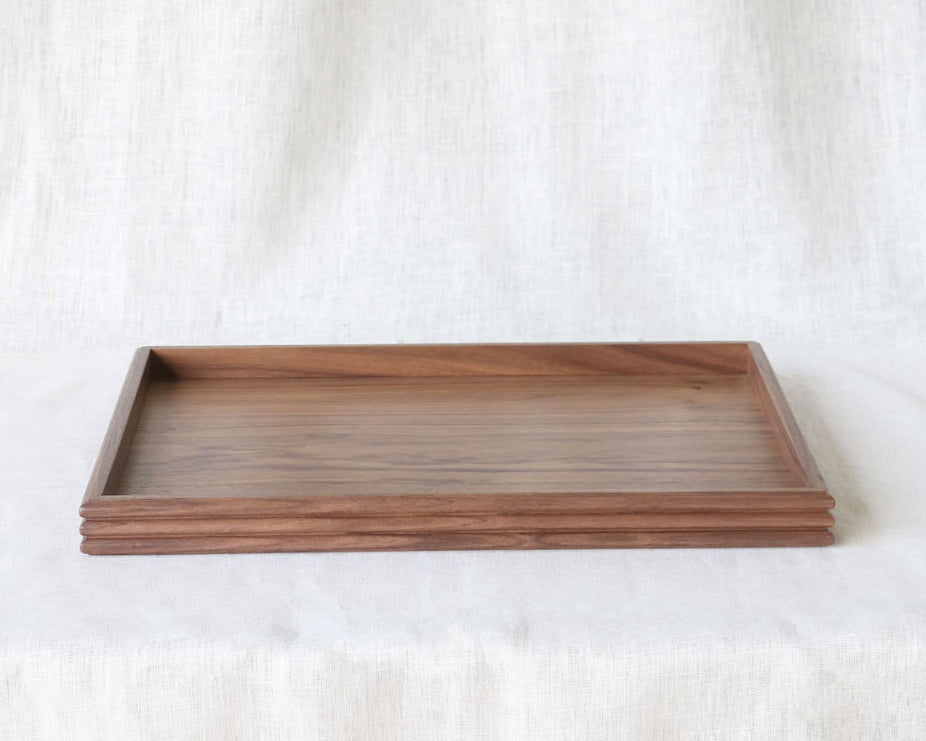 Front-facing image of the walnut tray on a table covered with light linen, displaying its compact, functional form and elegant craftsmanship.