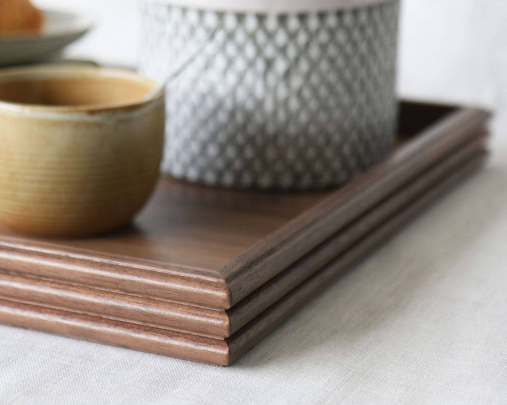 Close-up of the tray’s corner, capturing the reeded detailing, warm walnut tone, and part of the styled scene with a ceramic cup and textured plant pot.