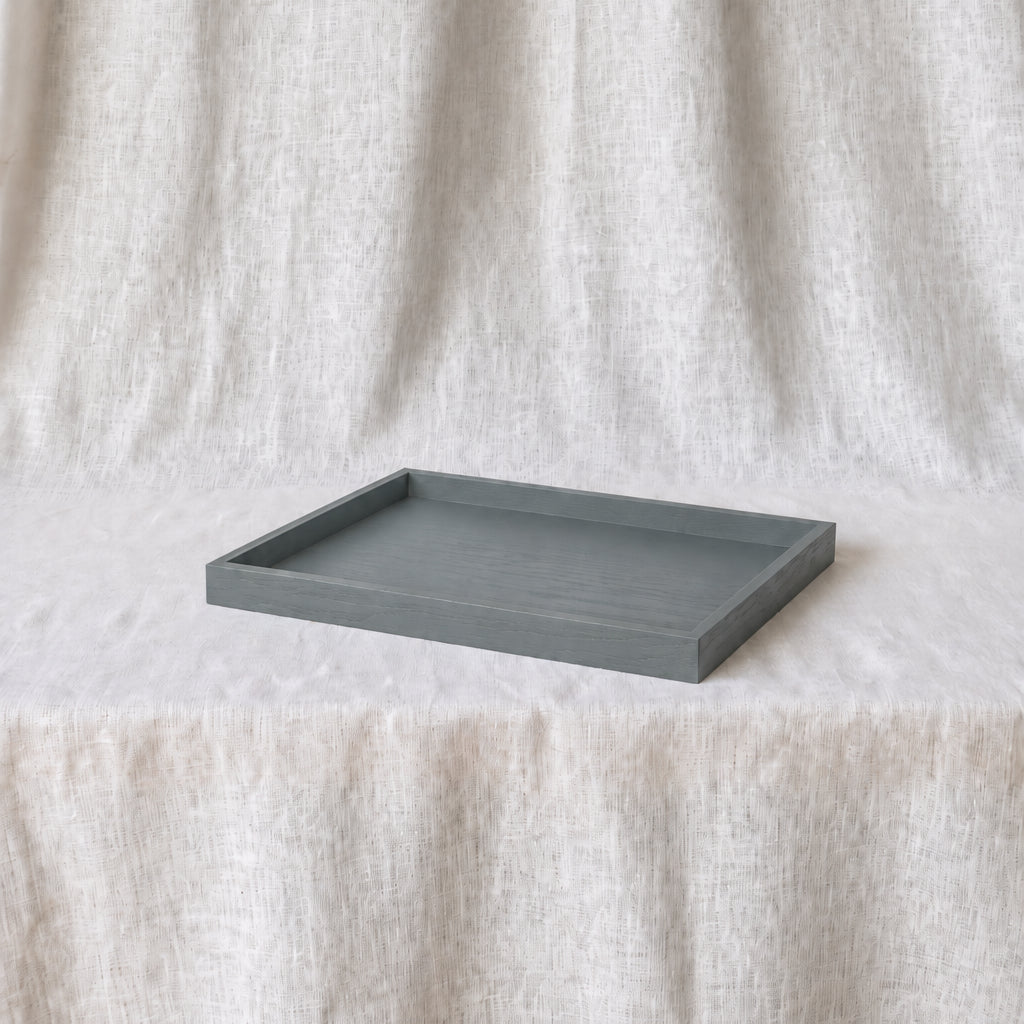 A rectangular dark grey tray with raised edges, placed on a textured cream fabric backdrop.
