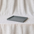 A rectangular dark grey tray with raised edges, placed on a textured cream fabric backdrop.